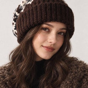 May include: A chunky knit beanie featuring a wide, solid dark brown ribbed cuff and a crown patterned with a geometric design in shades of dark brown, cream, and black. The hat is constructed from thick yarn with a visible, textured stitch pattern.