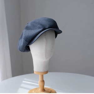 Peut inclure: Un béret bleu en velours côtelé à motif rayé. Le béret est sur une tête de mannequin blanche.