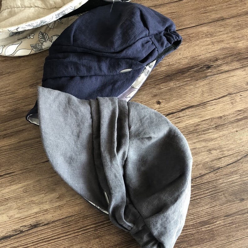 May include: Two linen sun hats, one navy blue and one gray, are folded and placed on a wooden surface.