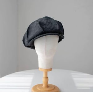 May include: A gray newsboy cap with a textured fabric. The cap is on a white mannequin head.