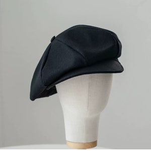 Op de afbeelding: Een zwarte newsboy-pet met een licht gebogen rand. De pet is gemaakt van een zachte, gestructureerde stof.