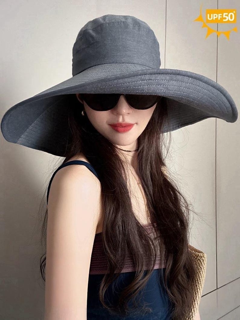 May include: A wide-brimmed, gray sun hat with a UPF50 rating. The hat features a structured crown and a broad, floppy brim. The image also shows black sunglasses.