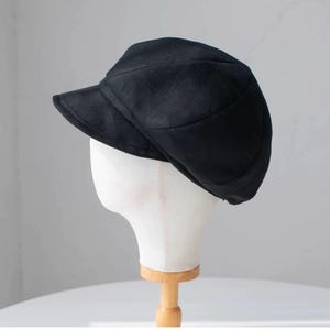 Puede incluir: Una gorra de newsboy negra con una visera ligeramente curvada. La gorra est&aacute; hecha de un tejido suave y texturizado.
