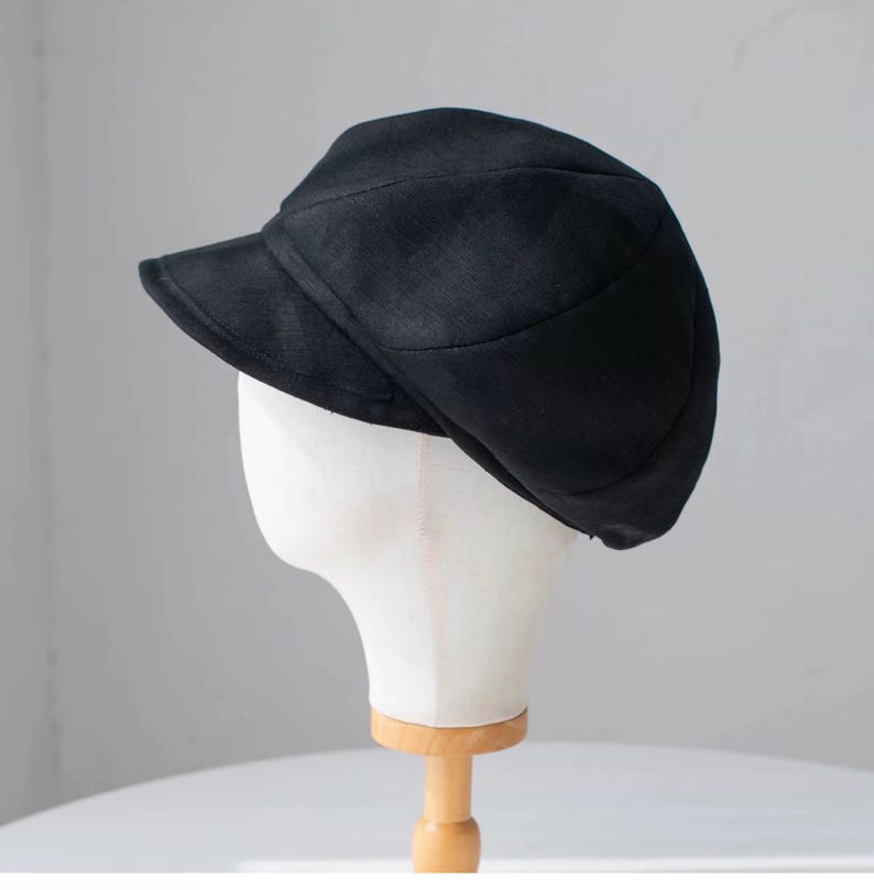 Puede incluir: Una gorra de newsboy negra con una visera ligeramente curvada. La gorra est&aacute; hecha de un tejido suave y texturizado.