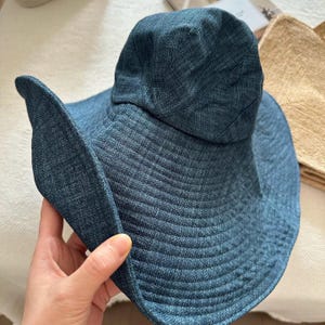 May include: A denim blue sun hat with a wide, floppy brim. The hat has a structured crown and a textured fabric. The brim is curved and provides ample shade. The hat is a stylish accessory for sunny days.