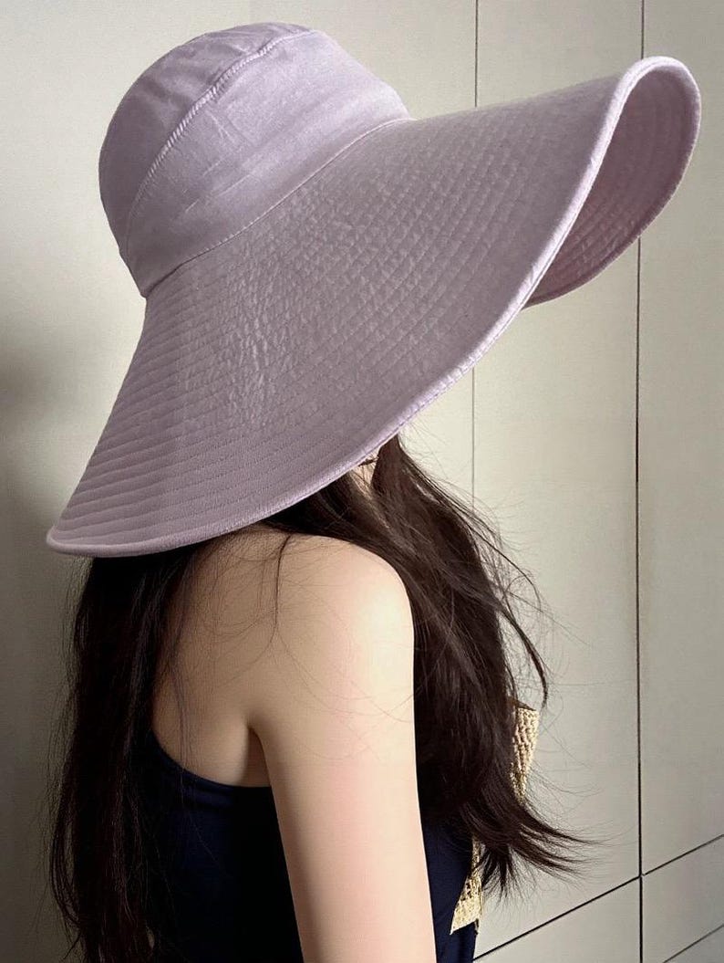 May include: A light purple sun hat with a wide brim. The hat has a textured appearance and a rounded crown. The brim is curved, providing ample shade. The hat is made of a lightweight material, suitable for sunny days.
