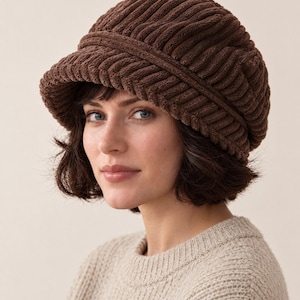 May include: A dark brown newsboy cap crafted from a thick, ribbed corduroy fabric. The hat features a rounded, voluminous crown and a structured, curved brim that extends from the front, showcasing a consistent vertical texture throughout.