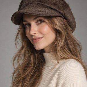 Può includere: Un berretto in stile newsboy marrone scuro con un aspetto testurizzato e infeltrito. Il cappello presenta una corona arrotondata composta da più pannelli e una visiera corta e rigida che si estende dalla parte anteriore.