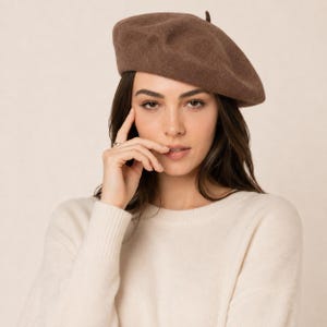 May include: A solid brown felt beret with a small, centred top tab. The hat features a smooth, uniform texture and a rounded, classic shape that sits comfortably on the head, providing a simple and clean look for any seasonal wardrobe.