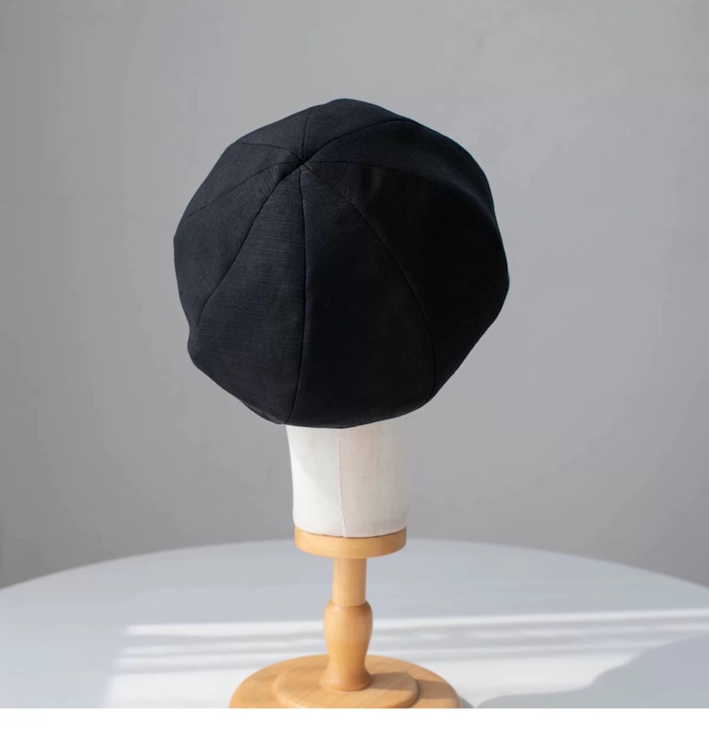 Puede incluir: Un gorro de boina negro en un soporte de madera. El gorro est&aacute; hecho de una tela suave y texturizada.