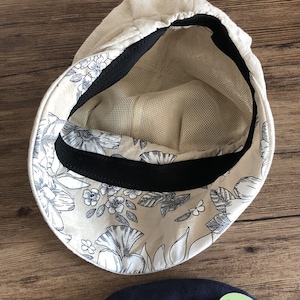 May include: A beige linen cap with a black elastic band and a floral print lining. The cap has a mesh lining.