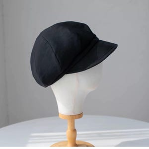 Puede incluir: Una gorra de newsboy negra con una visera ligeramente curvada. La gorra est&aacute; hecha de un tejido suave y texturizado.