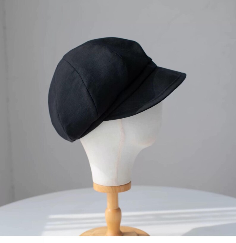 Puede incluir: Una gorra de newsboy negra con una visera ligeramente curvada. La gorra est&aacute; hecha de un tejido suave y texturizado.