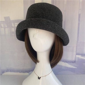 May include: A grey felt bucket hat with a wide brim. The hat is on a mannequin with brown hair and a black butterfly necklace.
