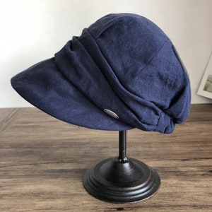 May include: A navy blue linen newsboy cap with a wide brim and a silver button detail.