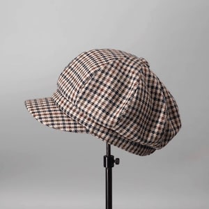 May include: A brown, black, and white checkered newsboy cap with a slightly curved brim.