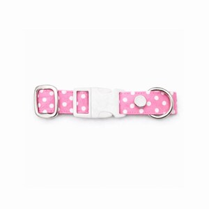 May include: Pink dog collar with white polka dots. The collar has a white plastic buckle, a silver metal D-ring, and a silver metal loop. The collar is designed for pets.