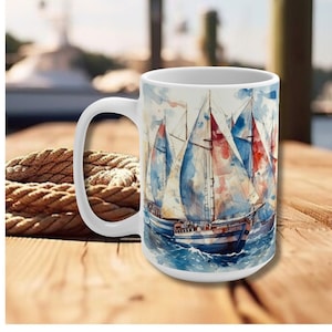 May include: White ceramic mug with a watercolor design of sailboats on the ocean. The sailboats have red, white, and blue sails.