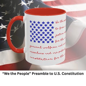 Könnte beinhalten: Eine weiße Keramik-Kaffeetasse mit rotem Rand und Henkel. Die Tasse zeigt ein blaues Sternenmuster und den Text "We the People" aus der Präambel der US-Verfassung.