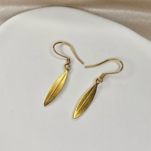 May include: A pair of gold leaf-shaped earrings with a simple design. The earrings are on a white surface.