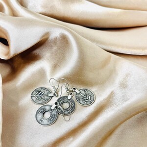 May include: Silver coin earrings with a leaf design and the words "One Mil" and "One Cent" on the coins.