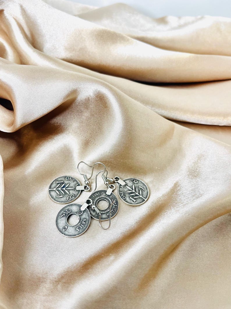 May include: Silver coin earrings with a leaf design and the words "One Mil" and "One Cent" on the coins.