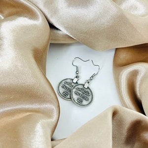 May include: Silver earrings with a round coin design featuring the word "Palestine" in both English and Arabic. The coins are attached to silver hooks.