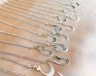 May include: A collection of silver necklaces with intricate Arabic calligraphy pendants. The necklaces are arranged in a row on a light brown fabric background.