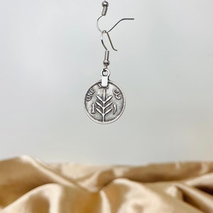 May include: Silver dangle earrings featuring a coin with a tree branch design and the words "ONE" and "1" on it.