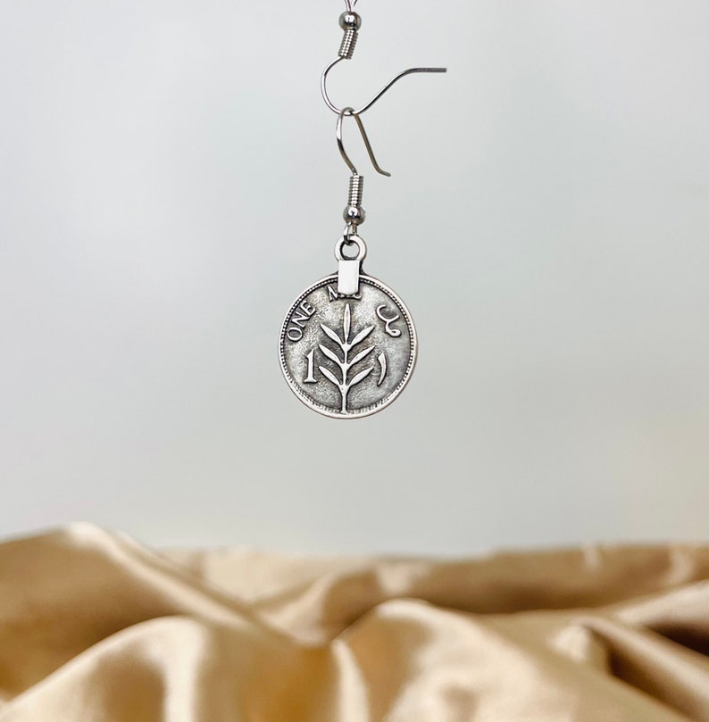 May include: Silver dangle earrings featuring a coin with a tree branch design and the words "ONE" and "1" on it.
