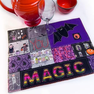 Può includere: Una brocca in ceramica arancione, una ciotola rossa e un calice su una superficie bianca. Un sottopentola patchwork con immagini di Halloween e la parola "MAGIC" in cuciture colorate. Il sottopentola ha uno schema di colori viola e nero.