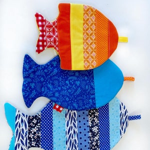 May include: Three colorful fish-shaped pot holders. The top pot holder is orange, yellow, and red with a geometric pattern. The middle pot holder is blue with a floral pattern. The bottom pot holder is blue with a striped pattern.