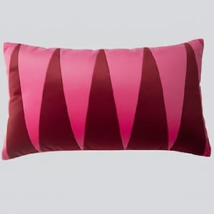 May include: A rectangular decorative pillow with a pink and burgundy geometric pattern. The pillow features a series of vertical, curved shapes in varying shades of pink and burgundy. The pillow is likely made of a soft fabric.