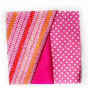 May include: A square of folded fabric featuring three distinct patterns. One section has a pink and orange striped design, another is solid magenta, and the third is pink with white polka dots. The fabric is likely for sewing or crafting.