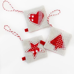 Könnte beinhalten: Drei handgemachte Weihnachtsornamente aus Leinenstoff mit roten und weißen gemusterten Stoffakzenten. Die Ornamente sind in Form eines Herzens, eines Sterns und eines Weihnachtsbaums.