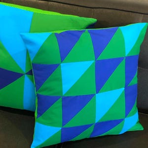 May include: Two decorative throw pillows featuring a geometric pattern of blue, green and turquoise triangles. The pillows are made from a soft, textured fabric.