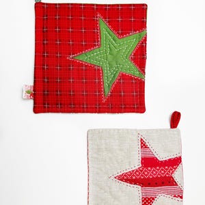 May include: Two red and white quilted pot holders with star designs. The top pot holder has a green star and the bottom pot holder has a red and white star.