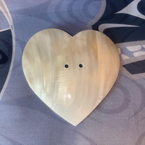 May include: A heart-shaped button made of white mother of pearl with two holes in the center.