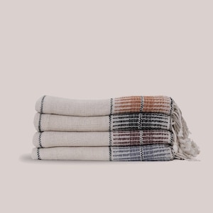 May include: A stack of four white towels with colorful stripes. The towels have a woven texture and fringe edges.