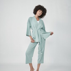 Model wearing a mint green matcha loungewear set, consisting of a wrap-style top with a side tie and three-quarter length sleeves, paired with comfortable, cropped pants.