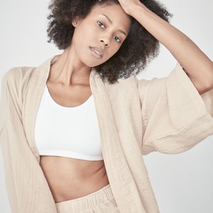 Model wearing a oat light beige yellow loungewear set, consisting of a wrap-style top with a side tie and three-quarter length sleeves, paired with comfortable, cropped pants.