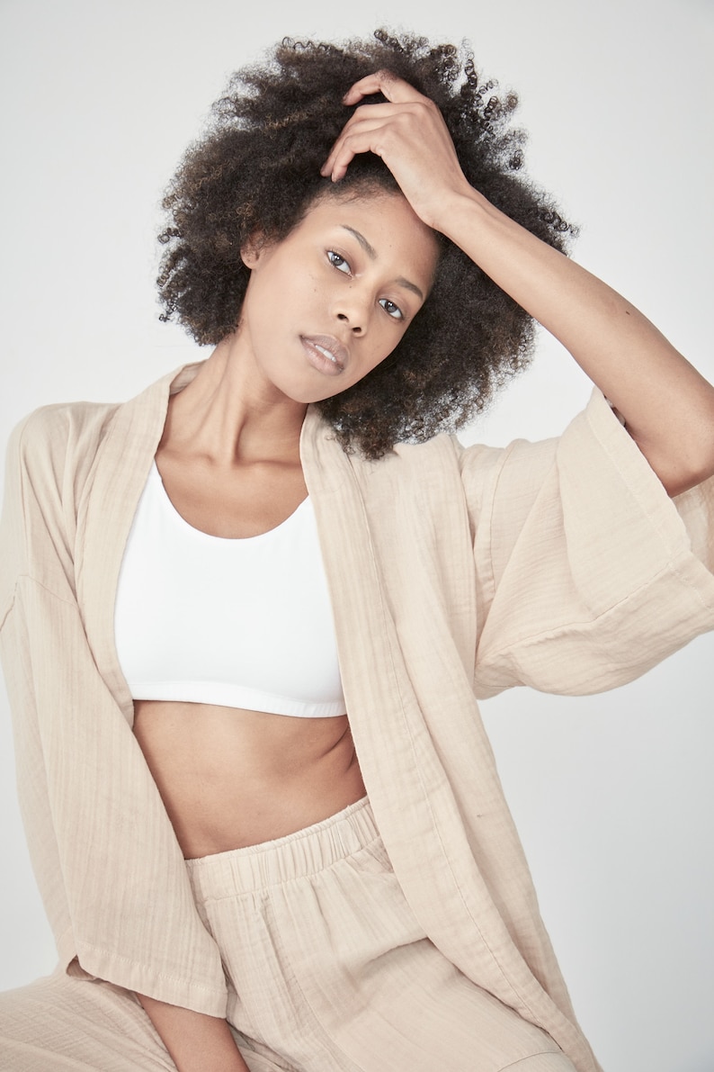 Model wearing a oat light beige yellow loungewear set, consisting of a wrap-style top with a side tie and three-quarter length sleeves, paired with comfortable, cropped pants.