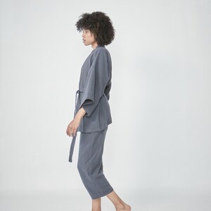 Model wearing a grey charcoal loungewear set, consisting of a wrap-style top with a side tie and three-quarter length sleeves, paired with comfortable, cropped pants.