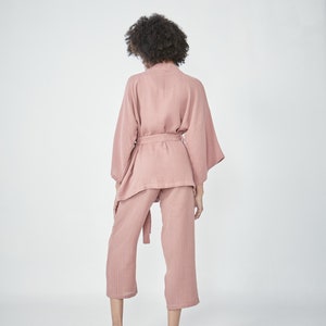 Model wearing a pink loungewear set, consisting of a wrap-style top with a side tie and three-quarter length sleeves, paired with comfortable, cropped pants.