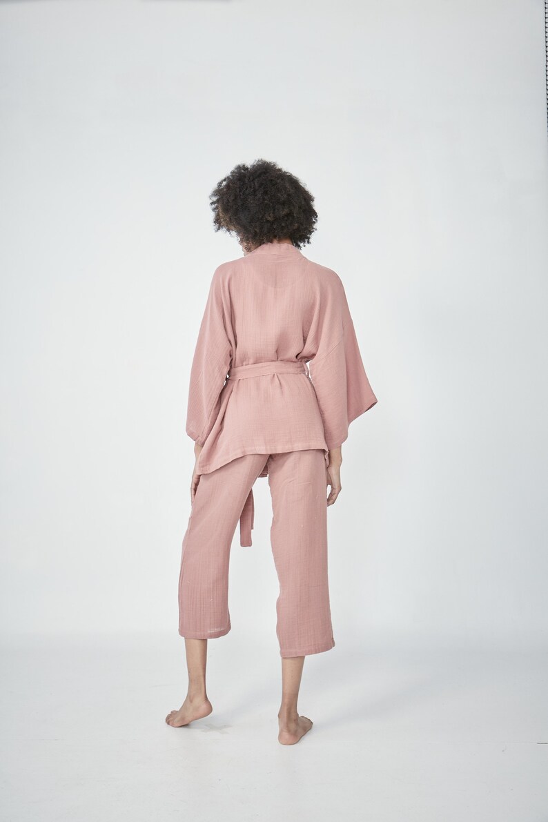 Model wearing a pink loungewear set, consisting of a wrap-style top with a side tie and three-quarter length sleeves, paired with comfortable, cropped pants.