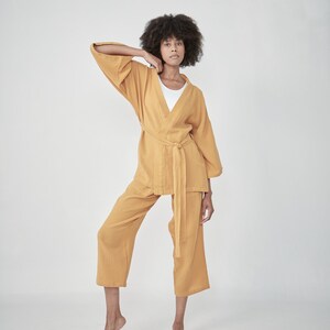 Model wearing a mustard yellow loungewear set, consisting of a wrap-style top with a side tie and three-quarter length sleeves, paired with comfortable, cropped pants.