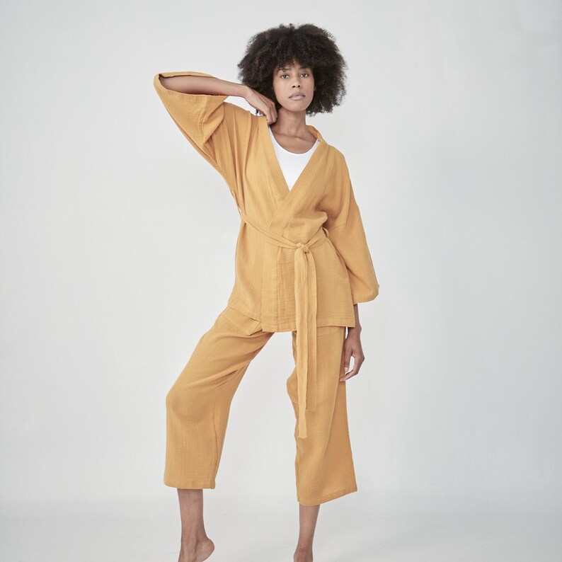 Model wearing a mustard yellow loungewear set, consisting of a wrap-style top with a side tie and three-quarter length sleeves, paired with comfortable, cropped pants.