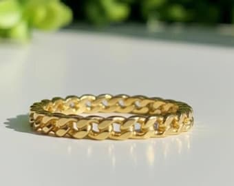 Könnte beinhalten: Ein goldfarbener Ring mit Kettengliedern. Der Ring besteht aus einer Reihe ineinandergreifender Glieder, die ein durchgehendes Band bilden. Der Ring liegt auf einer weißen Oberfläche mit verschwommenem grünem Hintergrund.