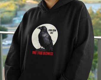 Puede incluir: Sudadera con capucha negra con un gráfico de un cuervo en un círculo con el texto "Doing Crow Shit" sobre el cuervo y "Mind Your Business" debajo del cuervo.