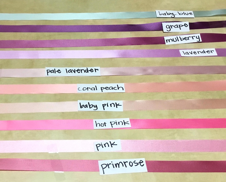May include: A collection of ten horizontal satin ribbons in various colors, each labeled with a white paper tag. The colors include baby blue, grape, mulberry, lavender, pale lavender, coral peach, baby pink, hot pink, pink, and primrose.
